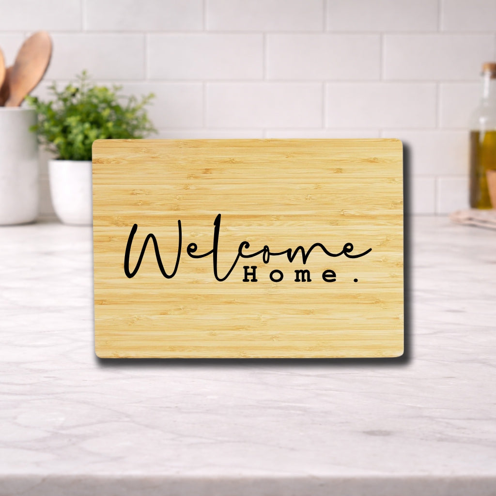 Engraved cutting board with the phrase "Welcome Home" displayed on a wooden surface in a kitchen setting.