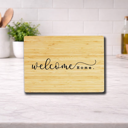 Engraved cutting board with the phrase "Welcome Home" displayed on a wooden surface in a kitchen setting.