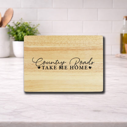 Engraved cutting board with the phrase 'Country Roads Take Me Home' on a wooden surface in a kitchen setting.
