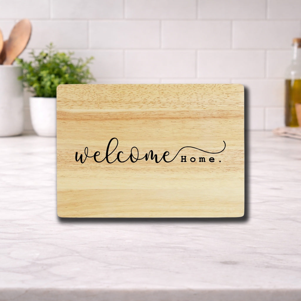 Engraved cutting board with the phrase "Welcome Home" displayed on a wooden surface in a kitchen setting.