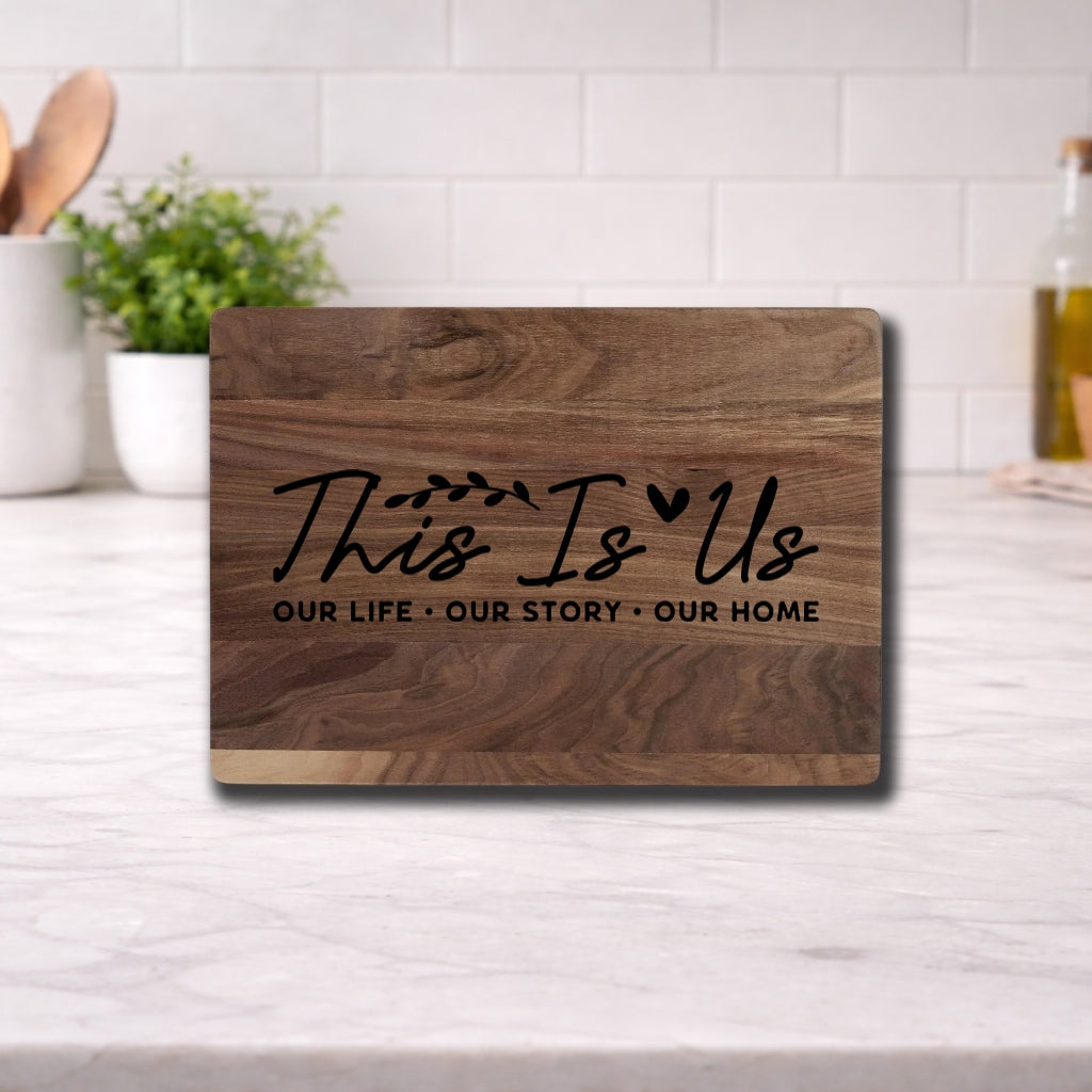 Engraved cutting board with the phrase 'This Is Us: Our Life, Our Story, Our Home' elegantly displayed.