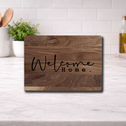 Engraved cutting board with the phrase "Welcome Home" displayed on a wooden surface in a kitchen setting.
